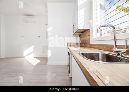 una cucina sotto una finestra con un ripiano in legno e controspruzzi dello stesso materiale in una casa vuota tipo loft Foto Stock