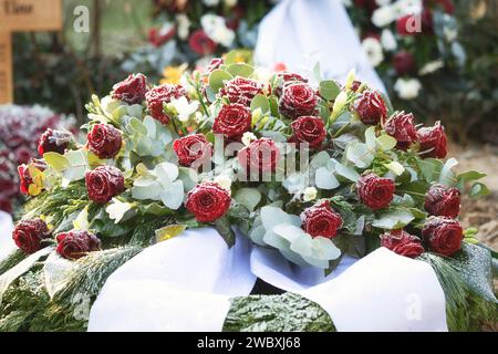 un bouquet di rose rosse con nastri bianchi come fiori funebri su una tomba coperta di cratere in inverno Foto Stock
