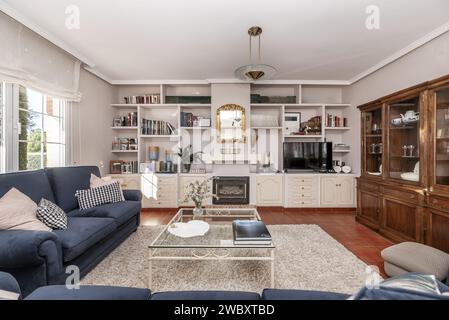 Immagine frontale del soggiorno di una casa unifamiliare con pavimenti in gres d'epoca, una libreria incorporata con porte e cassetti in legno bianco, e un b Foto Stock