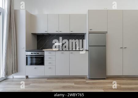 Immagine frontale di una cucina a pianta aperta in un appartamento loft con pavimenti in legno chiaro e splash back in marmo nero con venature Foto Stock