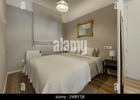 Una camera con un letto matrimoniale con copriletto bianco, cuscini a righe e pareti dipinte di grigio chiaro Foto Stock