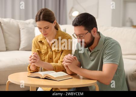 Coppia di famiglie che pregano per la Bibbia insieme a un tavolo al chiuso Foto Stock