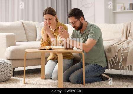 Coppia di famiglie che pregano per la Bibbia insieme a un tavolo al chiuso Foto Stock