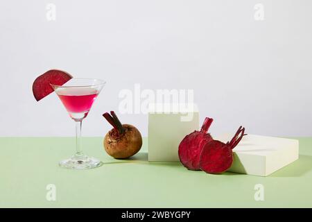 Podi bianchi a forma quadrata disposti con un bicchiere da cocktail di succo di barbabietola. Barbabietola (Beta vulgaris) può aiutare a trattare la pigmentazione con il suo vit Foto Stock