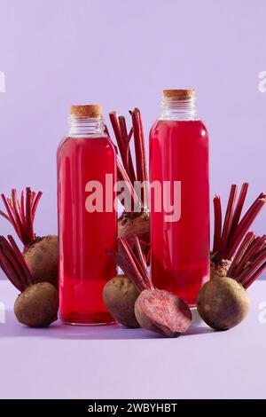 Vista frontale di due biberon senza etichetta contenente succo di barbabietola. Molte barbabietole in giro. Barbabietola (Beta vulgaris) potrebbe aiutare a mantenere il tuo bloo Foto Stock