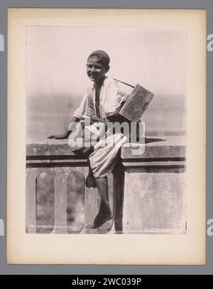 Ritratto di un ragazzo sconosciuto, presumibilmente un pulitore di scarpe, Alexandre Leroux (fotografo), 1880 - 1900 stampa fotomeccanica di Algeri. ragazzo collotipo di cartone (bambino tra il bambino e la giovinezza). calzolaio, ciabattino. anonimo personaggio storico ritratto Foto Stock