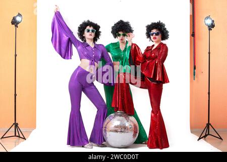 Un gruppo di ragazze con un ballo da discoteca in costumi colorati in uno studio fotografico in posa su sfondo bianco. Foto Stock