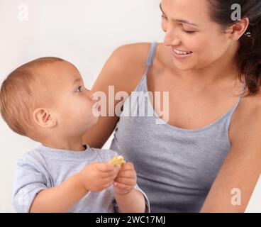 Incollaggio, letto e madre con biscotti che mangiano il bambino per uno spuntino delizioso e nutriente. Sviluppo del bambino, amore e giovane mamma con bambino, bambino Foto Stock