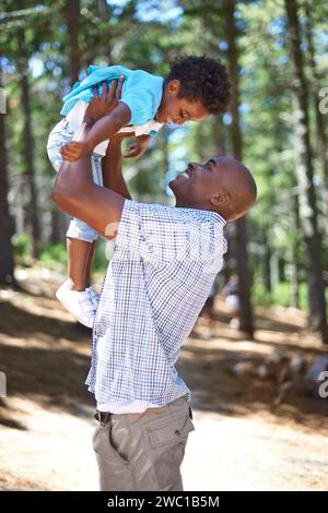 Giocare, papà e bambini nella foresta con sorriso, felicità e avventura nella natura per le vacanze estive sugli alberi. Bonding, uomo nero e figlio giocoso nel bosco Foto Stock