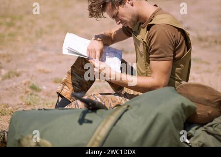 Uomo con mappa sul campo di battaglia, pianificazione del luogo di battaglia o obiettivi operativi tattici per missioni in guerra. Il soldato è all'aperto nel campo base militare, controlla Foto Stock