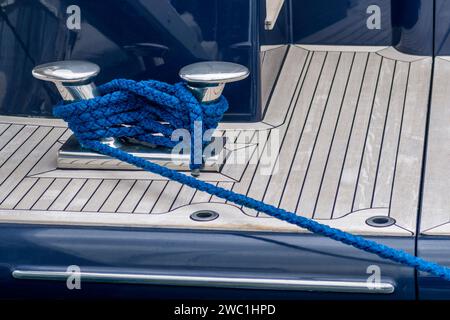 Tassello in acciaio inox con corda blu su un ponte di superyacht. La linea di ormeggio avvolta intorno ai bitts sul ponte del super yacht. Disposizioni di ormeggio. Foto Stock