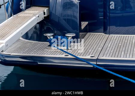 Tassello in acciaio inox con corda blu su un ponte di superyacht. La linea di ormeggio avvolta intorno ai bitts sul ponte del super yacht. Disposizioni di ormeggio. Foto Stock