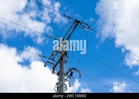 linea aerea a media tensione, asta con isolanti e sezionatori, nuvole bianche nel cielo blu Foto Stock