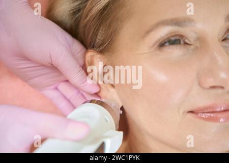 Primo piano del cosmetologo che fa il sollevamento rf microneedle della pelle dell'orecchio della donna Foto Stock