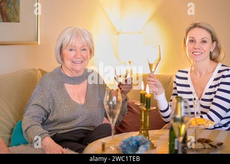 Madre e figlia sono sedute insieme sul divano e brindano con champagne Foto Stock