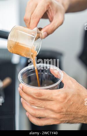 Il barista versa il caffè espresso dalla tazza dosatrice alla tazza di plastica nel bar Foto Stock