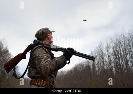 Un cacciatore con un fucile scaricato sulla spalla si trova al crepuscolo in una radura forestale. Guarda il becco maschio, che fa un corteggiamento Foto Stock