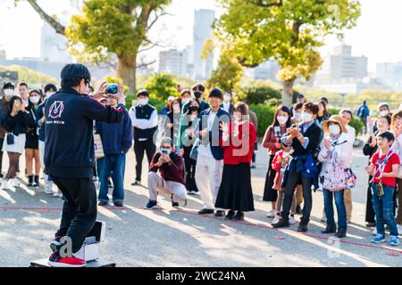 Giocoliere in piedi su un piccolo tavolo per intrattenere una piccola folla di persone che guardano il sole luminoso in una giornata primaverile al Parco del Castello di Osaka. Foto Stock