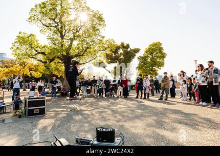 Giocoliere in piedi su un piccolo tavolo per intrattenere una piccola folla di persone che guardano il sole luminoso in una giornata primaverile al Parco del Castello di Osaka. Foto Stock