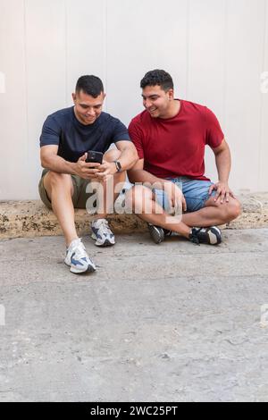 Due amici seduti e sorridenti mentre guardano uno smartphone insieme Foto Stock