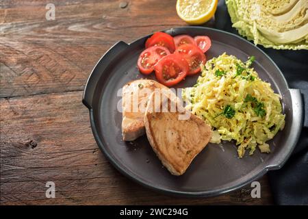 Bistecche di tonno fritte con cavolo savoy e pomodori su un piatto scuro e un tavolo rustico in legno, spazio per copiare, messa a fuoco selezionata, profondità di campo ristretta Foto Stock