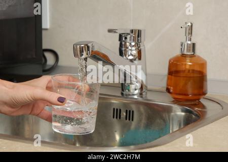 Riempire un bicchiere con acqua potabile dal rubinetto della cucina Foto Stock