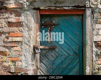 Una porta di legno verde in un vecchio fienile di mattoni con una serratura in metallo. Foto Stock