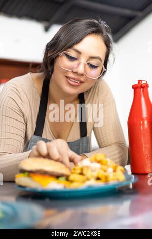 delizioso fast food e giovane donna sorridente, interno del ristorante con hamburger e patatine fritte, stile di vita e ritratto di bellezza, occupazione Foto Stock