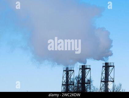 Tre camini di fabbrica contro un cielo blu con fumo. Foto Stock