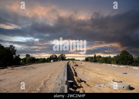 Costruzione di autostrade. Versamento di asfalto, installazione di barriere acustiche. Attrezzature per l'edilizia pesante in cantiere, rullo, escavatore, bulldozer Foto Stock