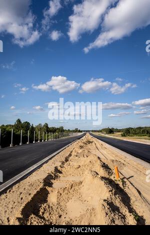 Costruzione di autostrade. Versamento di asfalto, installazione di barriere acustiche. Attrezzature per l'edilizia pesante in cantiere, rullo, escavatore, bulldozer Foto Stock