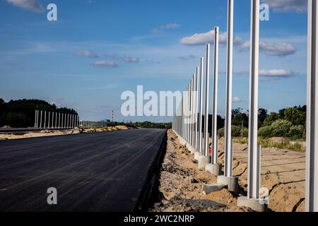 Costruzione di autostrade. Versamento di asfalto, installazione di barriere acustiche. Attrezzature per l'edilizia pesante in cantiere, rullo, escavatore, bulldozer Foto Stock