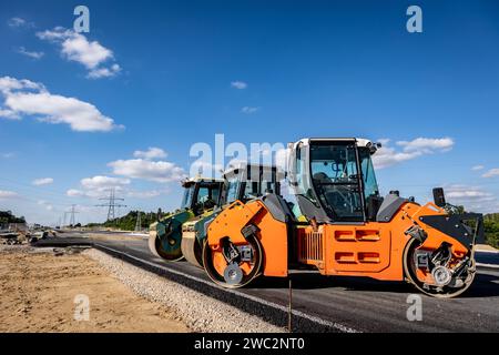 Costruzione di autostrade. Versamento di asfalto, installazione di barriere acustiche. Attrezzature per l'edilizia pesante in cantiere, rullo, escavatore, bulldozer Foto Stock