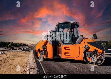 Costruzione di autostrade. Versamento di asfalto, installazione di barriere acustiche. Attrezzature per l'edilizia pesante in cantiere, rullo, escavatore, bulldozer Foto Stock