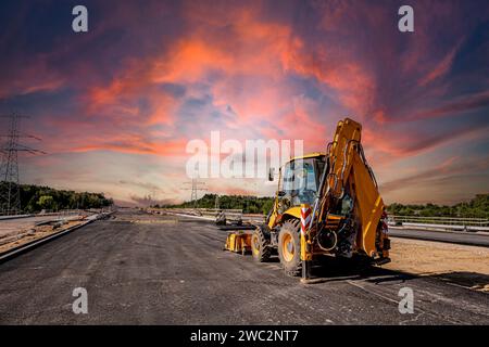 Costruzione di autostrade. Versamento di asfalto, installazione di barriere acustiche. Attrezzature per l'edilizia pesante in cantiere, rullo, escavatore, bulldozer Foto Stock