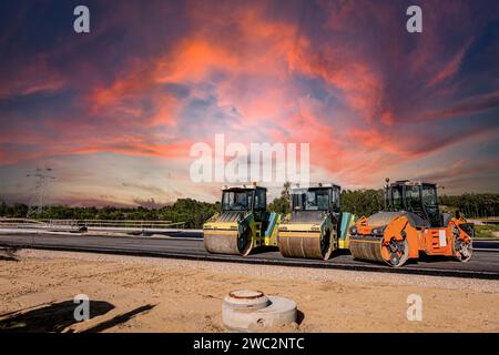 Costruzione di autostrade. Versamento di asfalto, installazione di barriere acustiche. Attrezzature per l'edilizia pesante in cantiere, rullo, escavatore, bulldozer Foto Stock