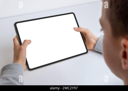 Primo piano delle mani di un ragazzo che tiene un tablet mockup. Impegnato nel lavoro, presenta uno schermo bianco isolato per la presentazione delle app. Tecnologia moderna per bambini Foto Stock