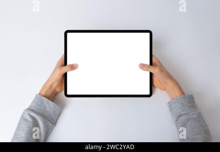 Vista dall'alto delle mani di un bambino che tiene un tablet orizzontale su una scrivania. Composizione piatta con schermo isolato per il mockup, perfetta per mostrare interi Foto Stock