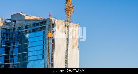 Ascensore con gru gialla collegato al lato dell'edificio in costruzione contro un cielo azzurro Foto Stock