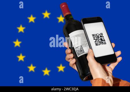 Etichettatura elettronica dei prodotti vitivinicoli nell'UE. La persona scansiona il codice QR sull'etichetta della bottiglia di vino utilizzando il telefono cellulare davanti alla bandiera anteriore dell'Unione europea. Foto Stock