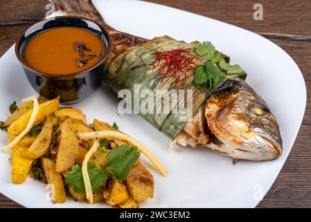 Pesce dorado al forno in foglie di bambù cosparse di coriandolo e fili di peperoncino, patate al forno e salsa Szechuan. Cucina casalinga. Foto Stock