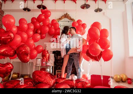 Un momento di gioia tra la danza di giovani coppie che festeggiano con un brindisi di San Valentino vicino a palloncini rossi. Donna che regge un bicchiere di vino, occhi coperti, uomo abbraccia, Foto Stock