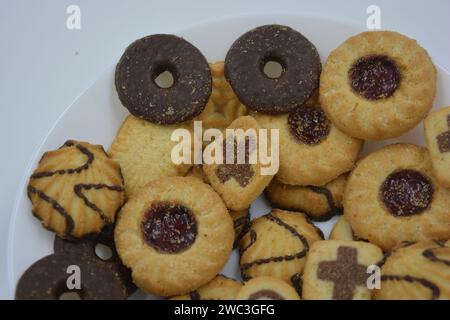 Un bellissimo e luminoso assortimento di biscotti di pasta frolla ricoperti di cioccolato e marmellata, di forme e tipi diversi. Prodotti da forno collocati su un bianco. Foto Stock