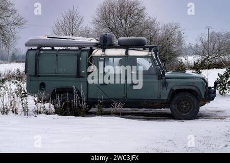 Defender Land rover d'epoca su fondo innevato. SUV Land Rover Defender d'epoca parcheggiato in un tranquillo paesaggio invernale coperto di neve fresca. La Foto Stock