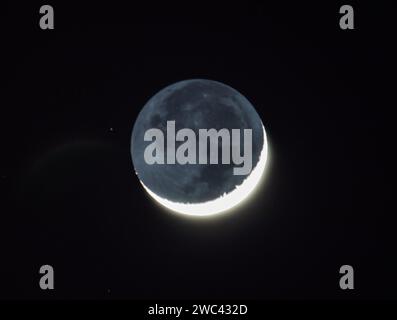 Una luna a mezzaluna con dettagli d'ombra affonda lentamente in un cielo notturno limpido il 13 gennaio 2024. Foto Stock
