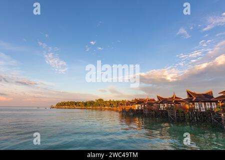 Capanne su palafitte si trovano sopra le limpide acque tropicali di un lussuoso hotel resort mentre il sole tramonta Foto Stock