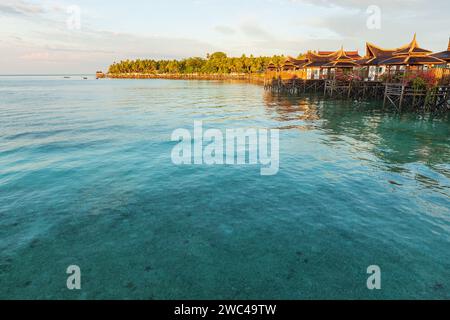 Capanne su palafitte si trovano sopra le limpide acque tropicali di un lussuoso hotel resort mentre il sole tramonta Foto Stock