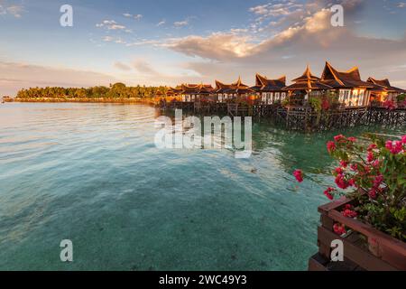 Capanne su palafitte si trovano sopra le limpide acque tropicali di un lussuoso hotel resort mentre il sole tramonta Foto Stock