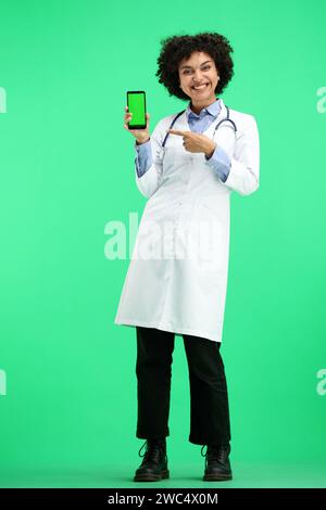 Medico donna, a tutta lunghezza, su sfondo verde, con un telefono Foto Stock