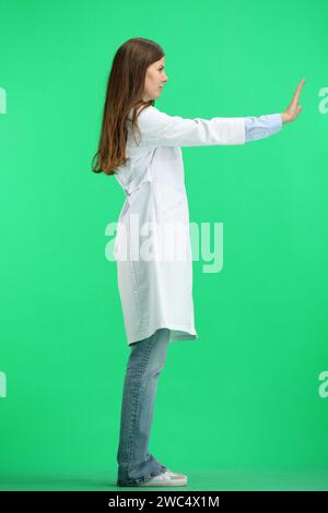 Una dottoressa donna, a tutta lunghezza, su sfondo verde, mostra un segnale di stop Foto Stock